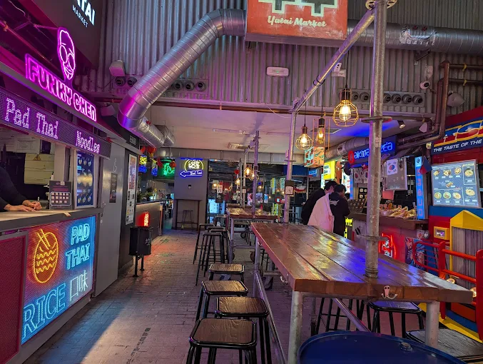 Interior de Yatai Market, restaurante asi&aacute;tico de moda en Madrid centro, con puestos de street food, carteles luminosos y ambiente urbano en la Calle del Doctor Cortezo 10.