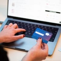 Persona pagando con tarjeta bancaria mientras usa un portátil, ilustrando la gestión de suscripciones online como ChatGPT Plus