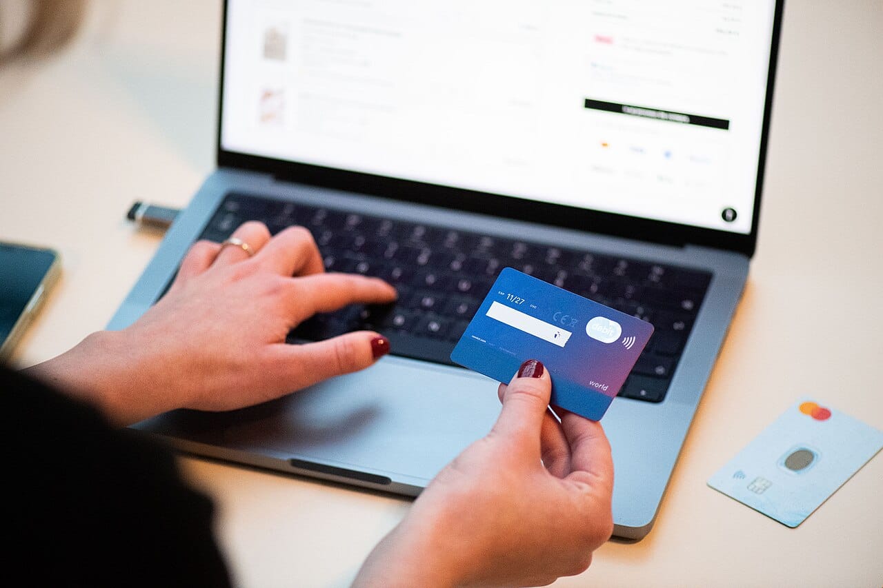 Persona pagando con tarjeta bancaria mientras usa un portátil, ilustrando la gestión de suscripciones online como ChatGPT Plus