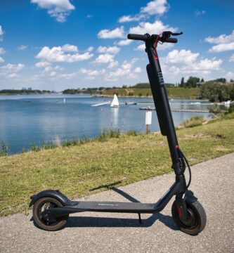 patinete eléctrico con batería extraíble apoyado en un carril junto a un lago