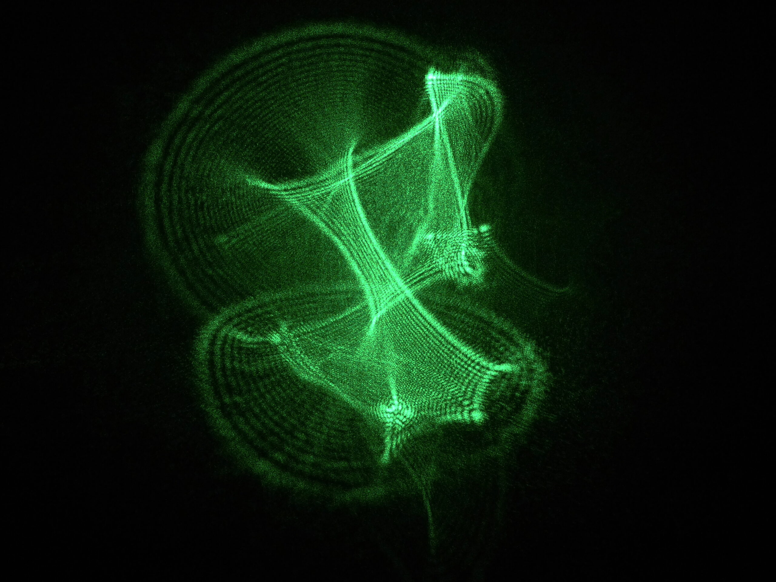 haz de láser verde atravesando un cristal irregular y proyectando un patrón ampliado y distorsionado