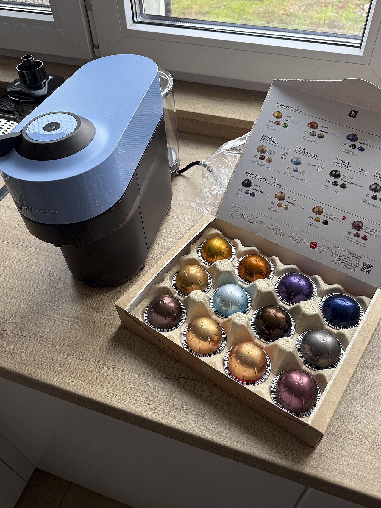 Cafetera Nespresso colocada en la encimera de una cocina junto a una caja de c&aacute;psulas