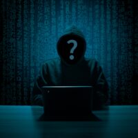 Hacker anónimo con sudadera y capucha frente a un portátil, con lluvia de código binario de fondo, representando el hacking ético y el bug bounty