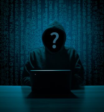 Hacker anónimo con sudadera y capucha frente a un portátil, con lluvia de código binario de fondo, representando el hacking ético y el bug bounty
