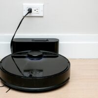 Robot aspirador negro cargando en su base junto a la pared, con espacio libre alrededor