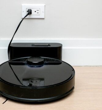 Robot aspirador negro cargando en su base junto a la pared, con espacio libre alrededor