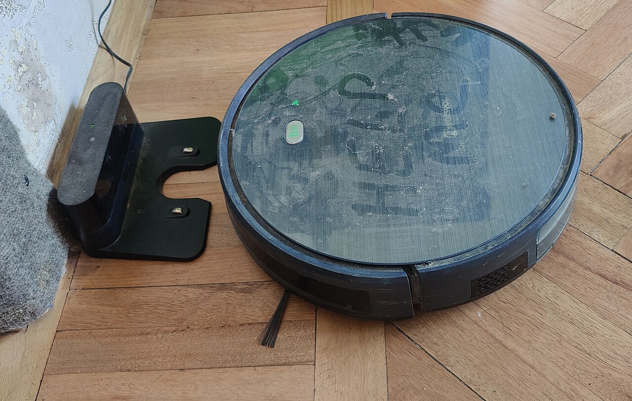 Robot aspirador junto a su base de carga con los contactos metálicos a la vista